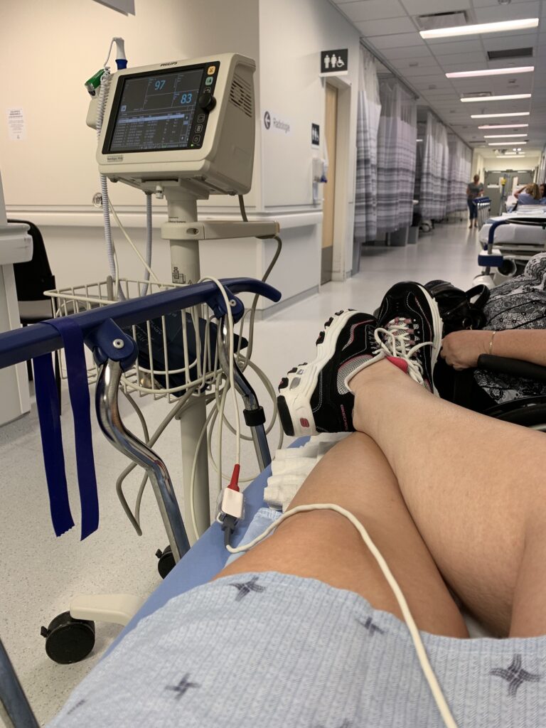 Photo des jambes d'une personne installée sur une civière dans un couloir d'urgences d'hôpital