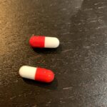 Deux capsules de médicament à moitié rouge et moitié blanc, sur table noire