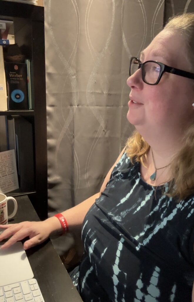 Annie-Danielle en pleine rencontre virtuelle. On voit une bibliothèque à côté d'elle et on devine un clavier d'ordinateur et une tasse à café sur le bureau devant elle.