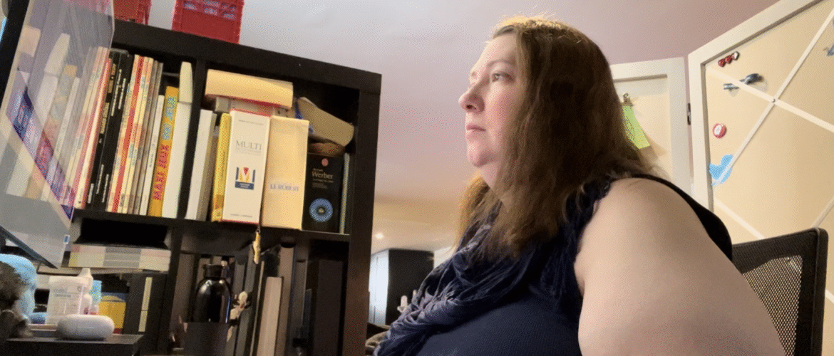 Annie-Danielle assise devant un écran d'ordinateur et qui tape sur un clavier, à côté d'une bibliothèque. On devine une tasse à café sur le bureau.